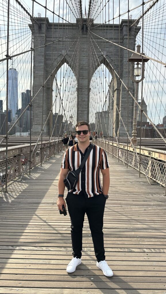 Kyle on the Brooklyn Bridge walkway in a striped knit shirt