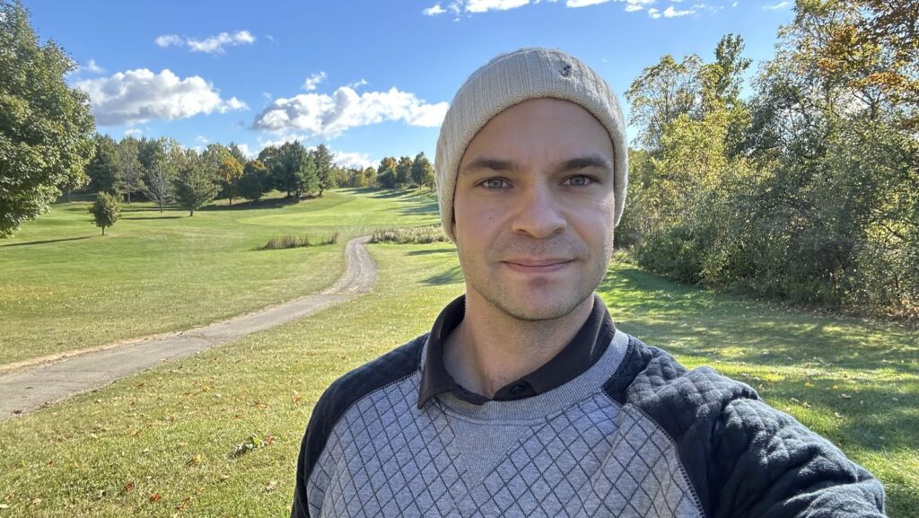 Kyle in a cream beanie on a sunny golf course