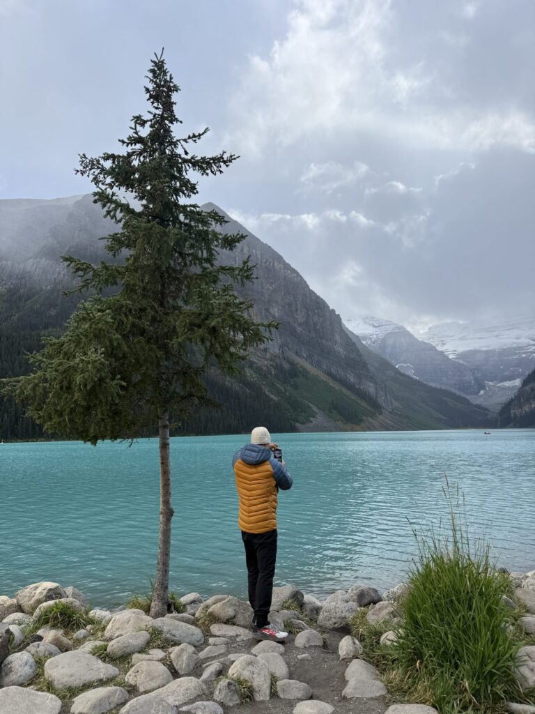 Kyle in an orange down jacket photographing a turquoise mountain lake